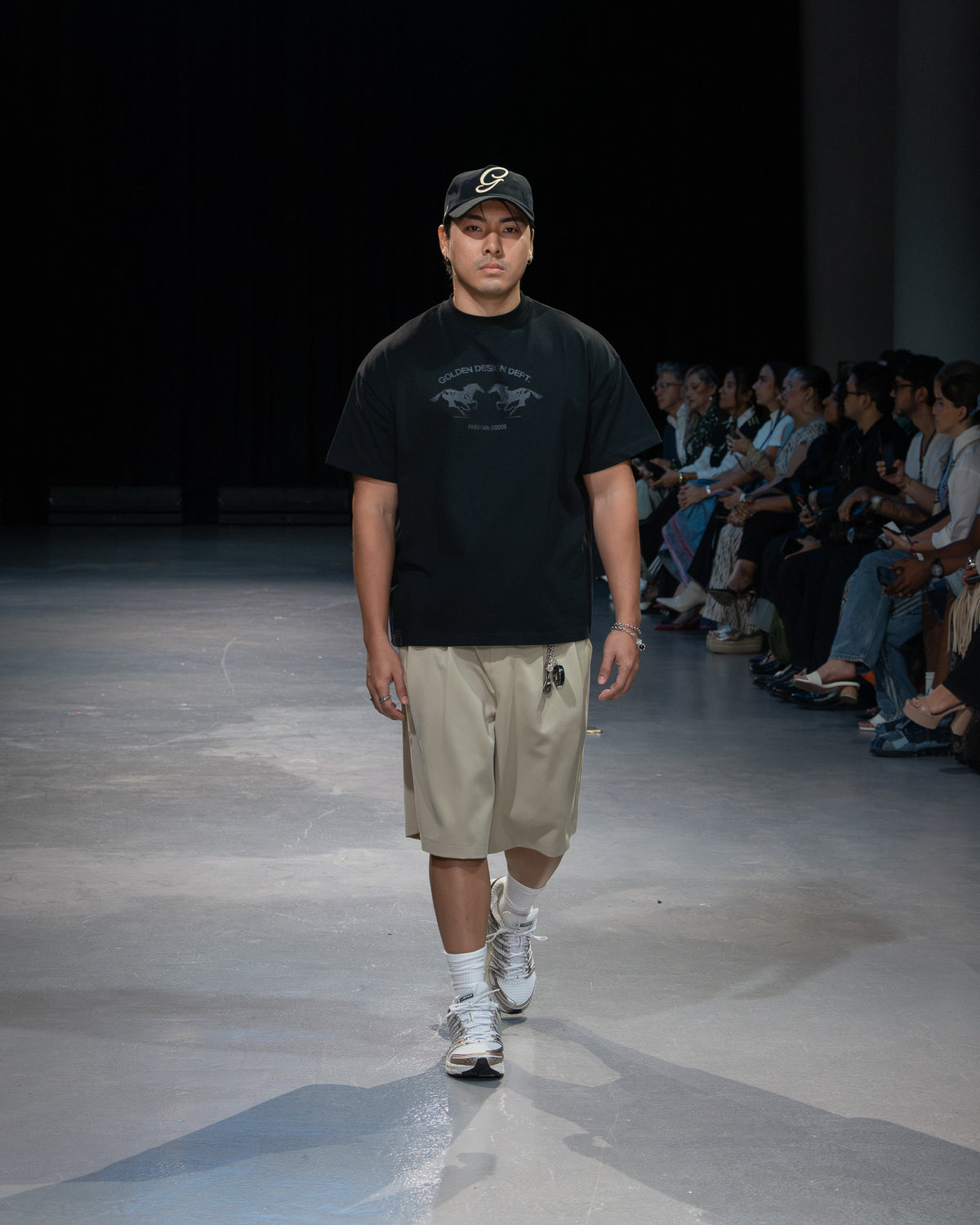 Golden Angels runway: Black graphic T-shirt, beige shorts and a script cap